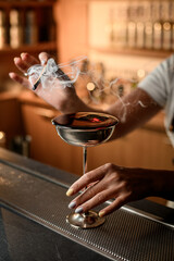 Female bartender holds a lighted wood chip in her hand and smokes it