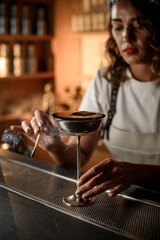 Focus on a metal glass with a tall thin stem filled with a cocktail, around which smoke from a wood chip spreads