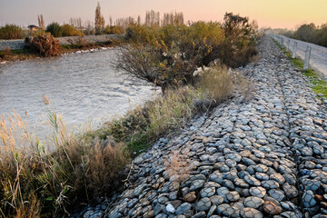 Gabions along a riverbank, stabilizing the shore with rocks encased in wire mesh.