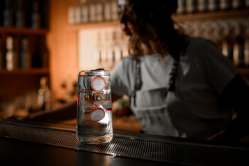 Glass with a clear cocktail, ice cubes and radish rings floating inside stands on a bar counter