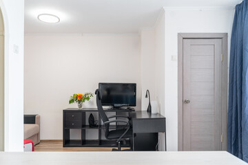 simple design in a modern apartment. A computer table and a chair. Black furniture. A vase of flowers on the chest of drawers