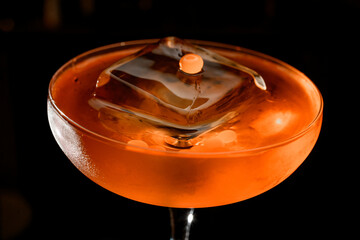 Close-up photo of the top of a glass filled with a brown cocktail with a huge ice cube that does not fit in the glass