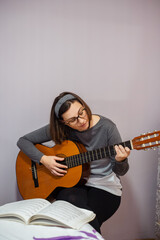 Woman playing acoustic guitar and reading music sheet at home