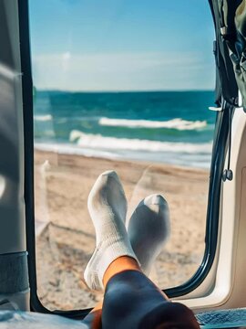 Relaxing beach day in a camper van - view of feet and ocean from inside the vehicle. Enjoying a peaceful seaside holiday with a scenic view of the sea, blue sky, and sandy beach, perfect for travel mo
