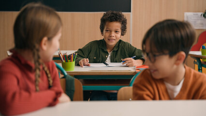 Multiracial diverse noisy little classmates multiethnic students pupils people children diversity kids friends noisy talking in school class at lesson sitting at table education learning studying talk