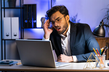 Tired ill Indian businessman suffering from headache problem tension and migraine, stress at home office desk workplace. Bearded freelancer broker worker man works on laptop notebook. Overworking