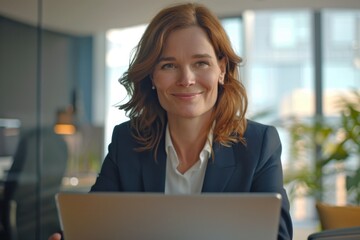 Woman smiling, working on laptop at office desk.