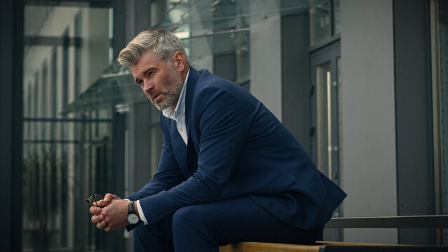 Pensive sad worried sorrowful thoughtful middle-aged man senior mature business employer businessman think ponder problem solution grief put on glasses dreaming contemplate thinking in city outdoors