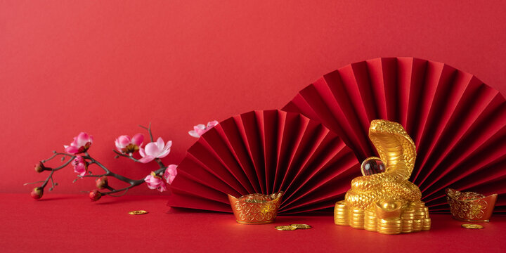 Festive image featuring a gold snake and red fans symbolizing Chinese New Year 2025. Red background enhances the cultural significance and prosperity theme, alongside floral, gold coin decorations - Powered by Adobe