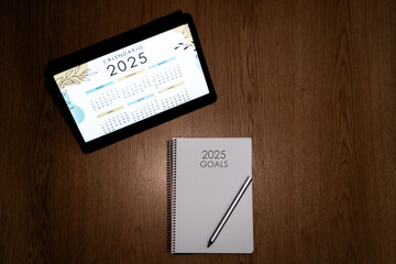 New Year's Goals 2025: Organized notebook on wooden desk with tablet in background