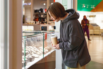 Middle aged woman looking at different casual clothes while shopping in mall
