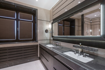 A modern bathroom with a window, a gray cabinet with sinks and a wide mirror.