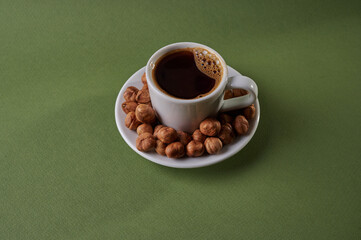 Enjoying a warm cup of coffee accompanied by roasted hazelnuts on a green tabletop in a cozy setting