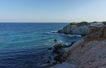 A serene coastal view showcasing rocky cliffs and tranquil waters at sunset near a hidden cove.