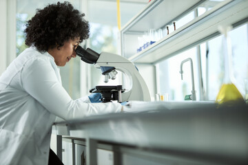 Side view of a female scientist looking through a microscope.