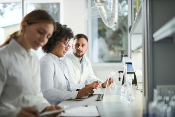 Team of biotechnologists cooperating while reading scientific data on a computer in laboratory.