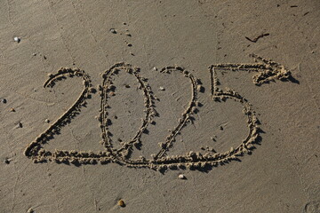 New Year 2025, lettering on the beach with wave and clear blue sea. Numbers 2025 year on the sea shore, message handwritten in the golden sand on beautiful beach background. New Years concept.