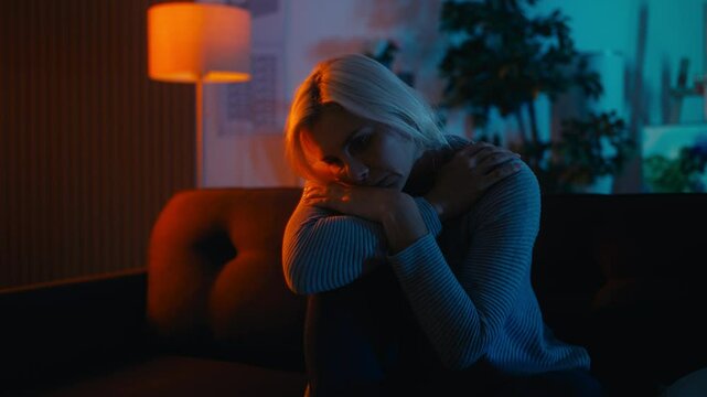 Stressed blond woman sitting alone on couch, rocking back and forth to calm down