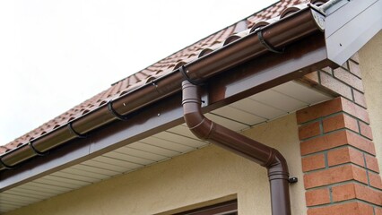 Brown PVC gutter attached to downpipe on roof edge, building feature, architectural detail, roof detail, guttering, brown pvc gutter