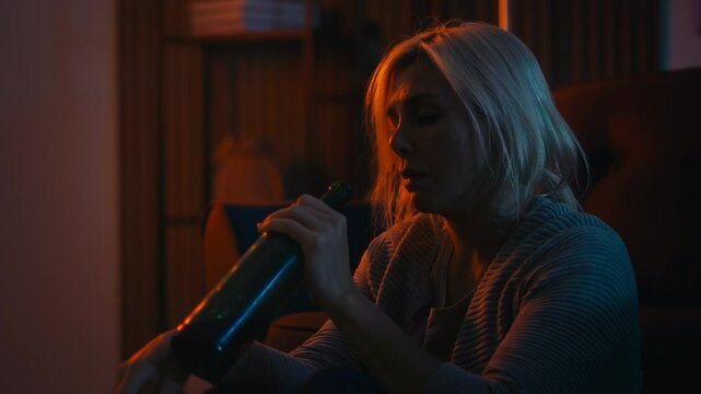 Upset blond woman sitting on the floor and drinking wine, healing mental wound