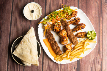 Turkish special mix grill with Chicken Tavuk, shish tawook, chicken kebab, ouzi chicken, Beef Adana, pita bread, hummus, and fries served in plate isolated on wooden table top view of turkish food