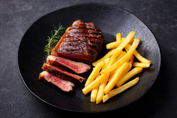 Beef Steak medium rare with French fries on a black plate. Dark background. Close up.