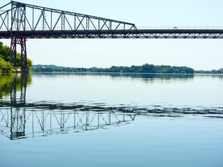 Serene lake waters reflected in the distance of a steel bridge with greenery on the other side, nature, calm