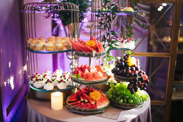 Fruits and sweets arranged on silver trays. Elegant food presentation on a banquet table. Sweet snacks displayed for guests at a restaurant. Decorative treats for a special occasion.