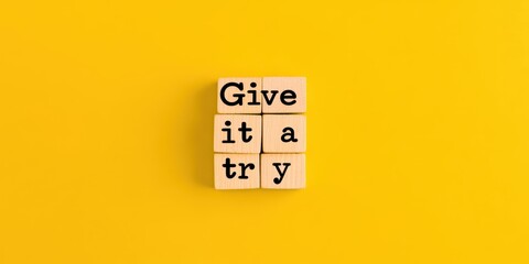 “Give it a try” message on wooden blocks with yellow background, motivational theme.