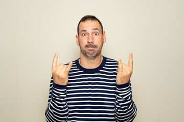 Portrait of bearded man showing rock and roll gesture, heavy metal sign, exclaiming with joy. Indoor studio photo isolated on beige background.