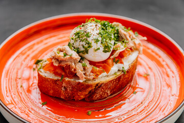 Delicious gourmet toast topped with poached egg, tuna, and fresh herbs on vibrant orange plate
