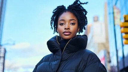 Stylish young black woman in a puffer jacket walking through a vibrant urban street on a bright winter day