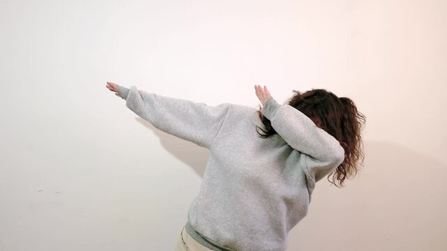 Trendy cheerful body positive young woman having fun dancing and moving to rhythm, making dub (dab) dance winner gesture. Happy girl isolated alone on white studio background. Lifestyles.