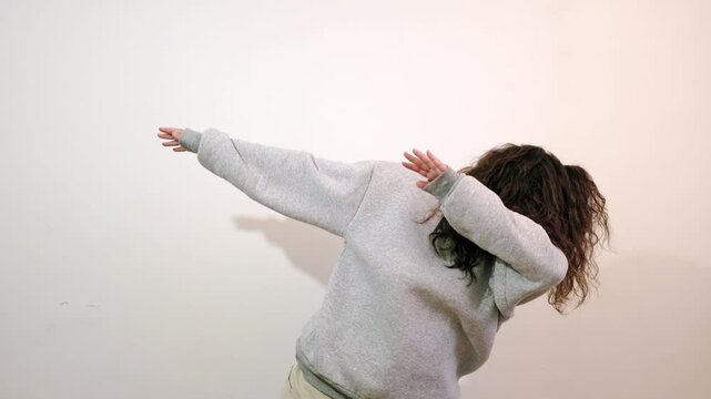 Trendy cheerful body positive young woman having fun dancing and moving to rhythm, making dub (dab) dance winner gesture. Happy girl isolated alone on white studio background. Lifestyles.