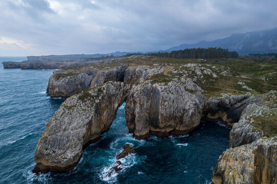 Aerial drone view of natural arch at Punta Pe&ntilde;a Flecha at sunset in Acantilados del Infierno near Ribadesella, Asturias, Spain. Wonder nature landscape with vivid sunset colors.