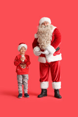 Santa Claus and cute little boy with milk and cookies on red background