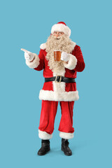 Santa Claus with mug of beer pointing at something on blue background