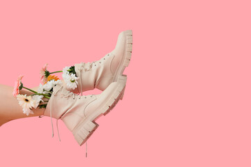 Legs of beautiful young woman in boots with flowers on pink background
