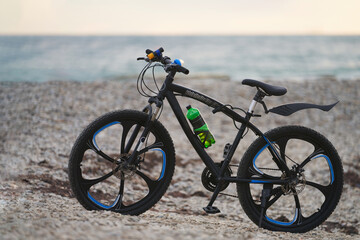 Fototapeta premium Two-wheeled bicycle with a drink bottle in a holder on a sea shingle beach. The background is blurred. Copy space.