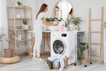 Young woman removing stain from clothes in sink at home