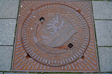 Rust-brown, iron manhole cover with the emblem and city name of the small Bavarian town of...