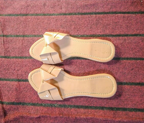 Beige sandals placed neatly on striped red doormat in flat lay view
