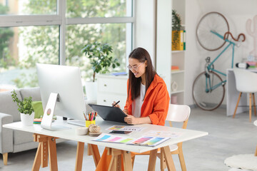 Young female graphic designer working with tablet at table in office