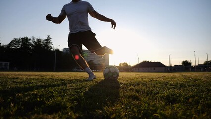 Silhouette of sportsman shooting a penalty kicks on stadium at sunset. Professional footballer kicking soccer ball at green field. Young man training at meadow. Concept of a freestyle football