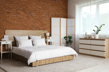 Interior of light bedroom with cozy bed and white folding screen