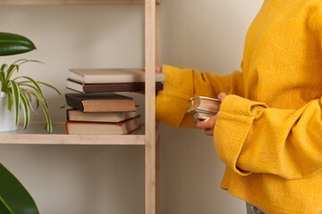 Young woman putting books on shelf in living room, closeup