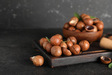 Wooden bowl and board with tasty macadamia nuts on black background