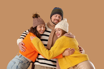 Man and two beautiful women in autumn clothes hugging on beige background. Polyamory concept