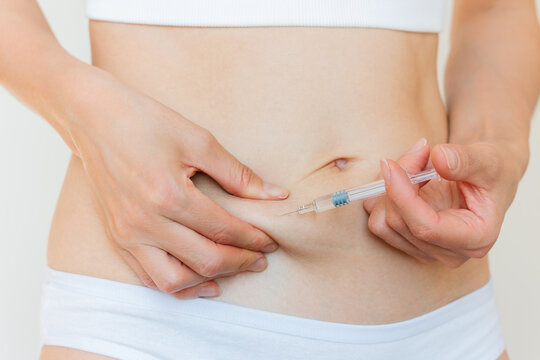 A young Caucasian woman in white underwear giving herself a subcutaneous injection into her stomach. Women's reproductive health. Trigger ovulation