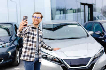 Happy man taking selfie through smart phone after purchasing new car. The man showing the purchased...